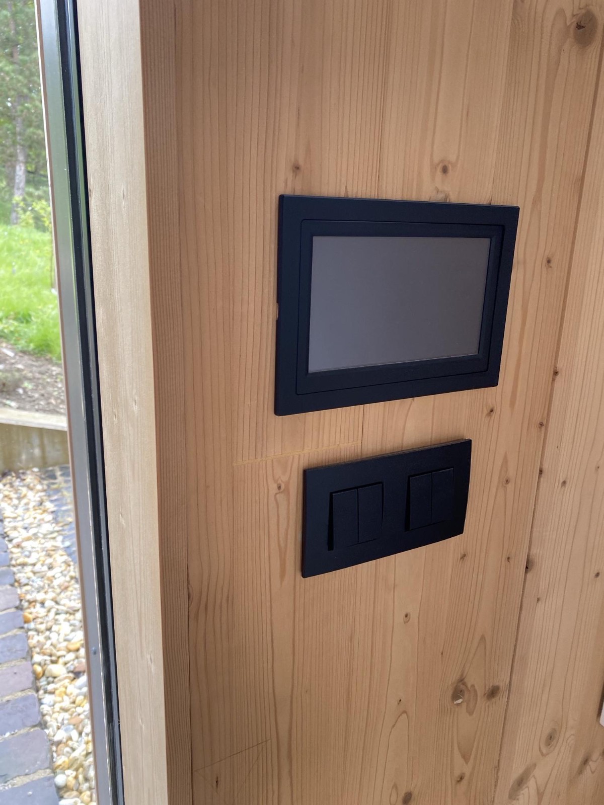 TapHome nástěnný panel a smart switch na dřevěné stěně s výhledem na zahradu