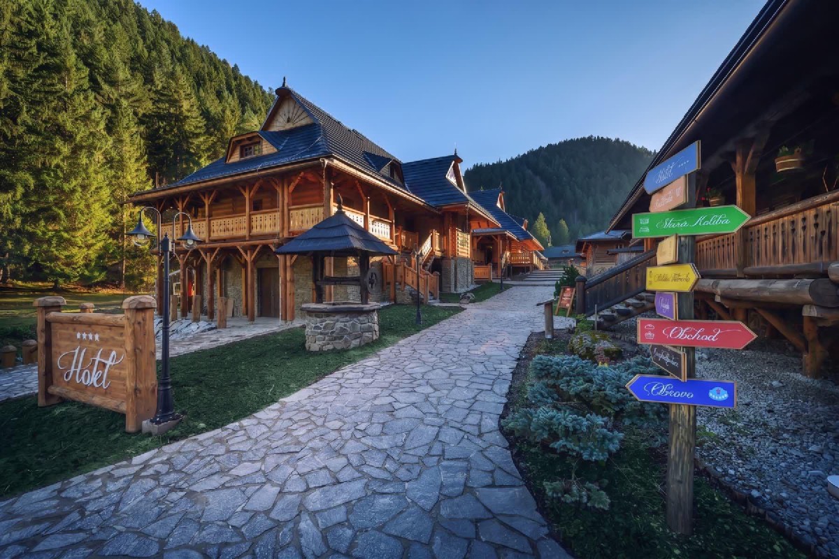 Hotel u dobrého pastiera nyáron — fa chalet kőlábazaton, az előtérben útjelző tábla a komplexum további objektumaira (Stará Koliba, wellness, hotel)