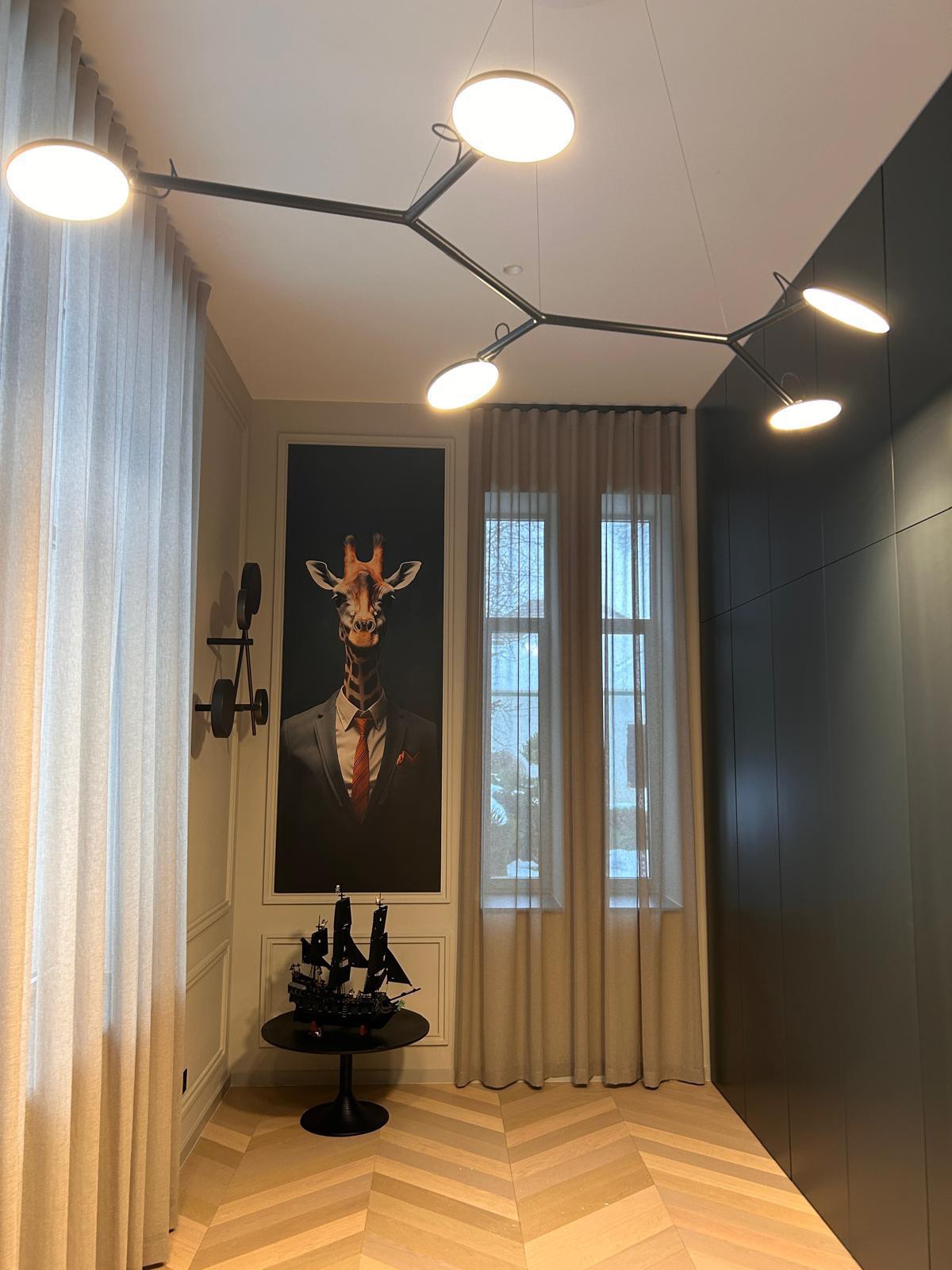 Előszoba szobrászati ágszerkezetű designer mennyezeti lámpával és zsiráf portré műalkotással