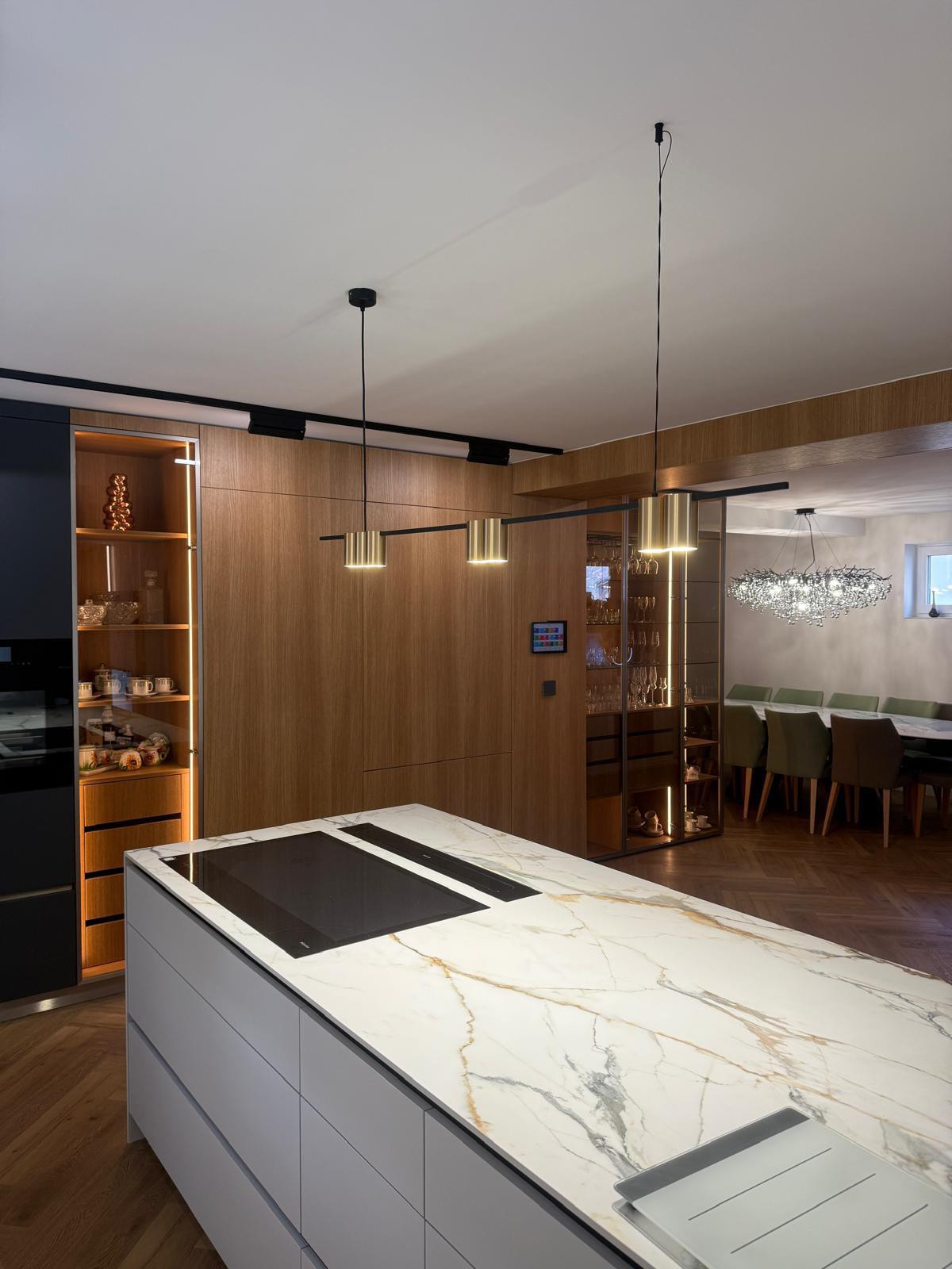 Moderní kuchyně s mramorovým ostrůvkem, LED podsvícenou vitrínou a výhledem do jídelny s křišťálovým lustrem