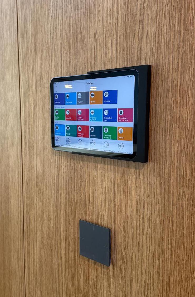 TapHome tablet na dubovém nástěnném panelu s barevným dashboardem a smart switchem pod ním